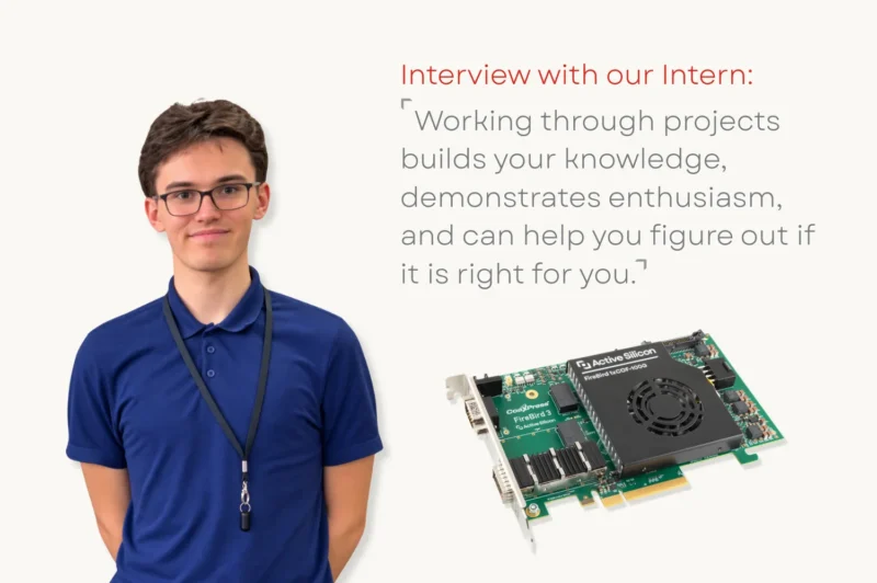 A student smiling at the camera next to a coaxpress over fiber frame grabber