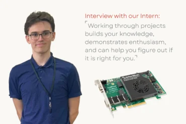 A student smiling at the camera next to a coaxpress over fiber frame grabber