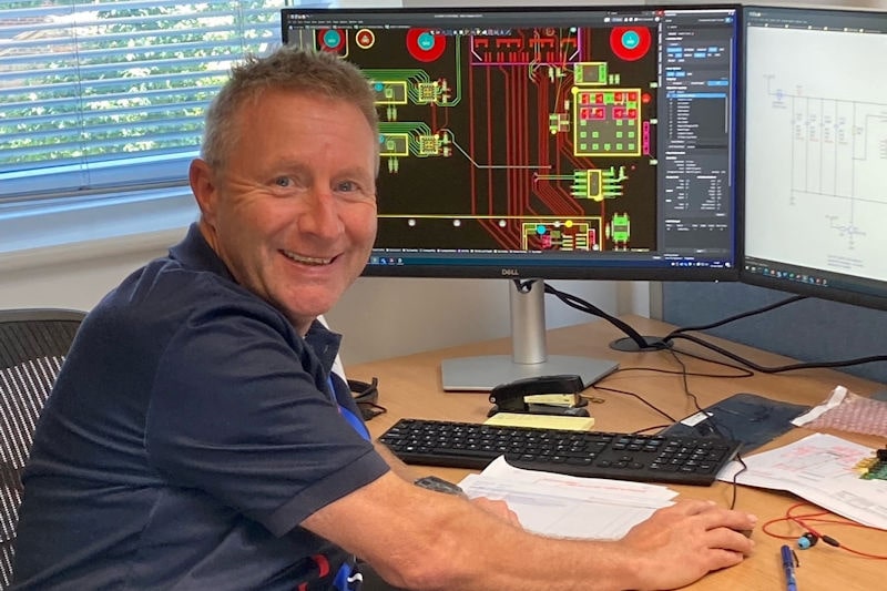 An engineer sitting at a computer with PCB design on the screen