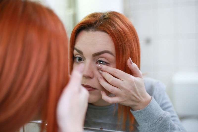 Lady looking in a mirror while inserting a contact lens