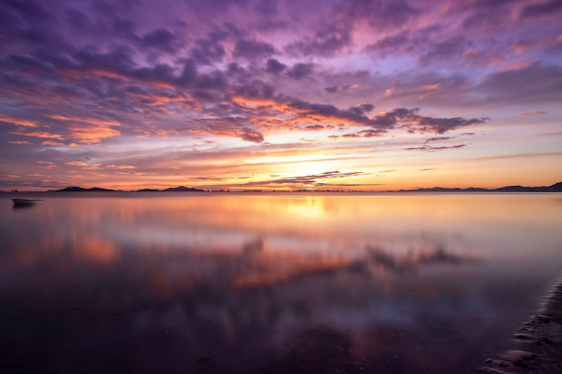 Colorful sunrise over water with a cloudy sky